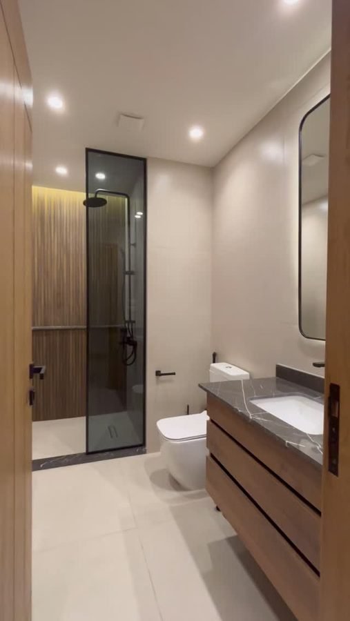 Black-framed shower, stone vanity. Fluted timber wall with concealed lighting